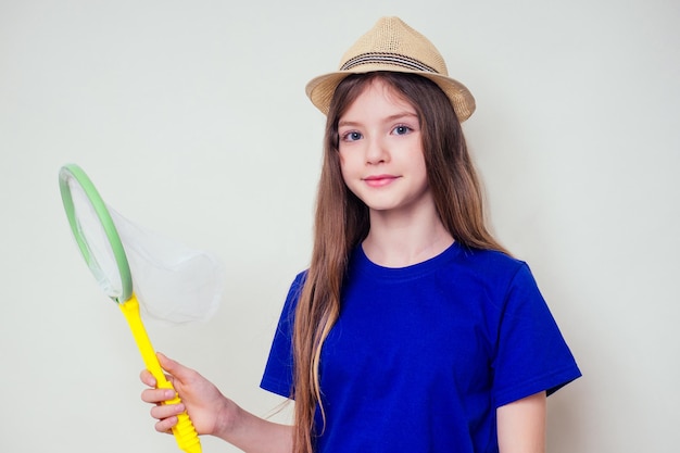 Niña adolescente pequeña y hermosa en un sombrero de paja sostiene un cazamariposas en su mano y atrapa mariposas estudio fondo blanco. Niño femenino alegre jugando