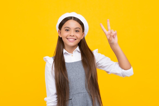 Niña adolescente de pie sobre un fondo amarillo aislado mostrando los dedos haciendo el signo de la victoria Vsign número dos Niña feliz cara emociones positivas y sonrientes