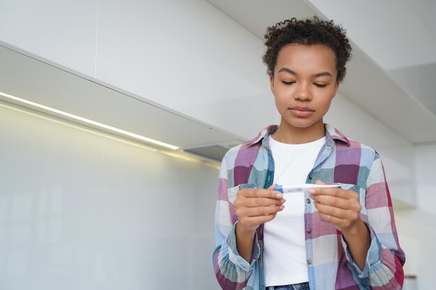 Niña adolescente de raza mixta malsana comprueba la temperatura corporal con un termómetro digital de pie en casa