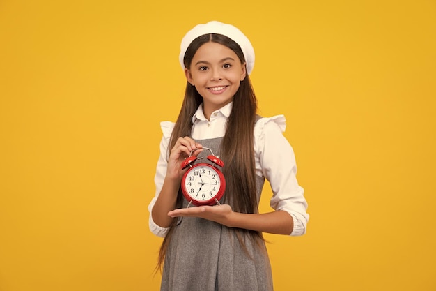 Niña adolescente con reloj de alarma aislada en fondo amarillo Concepto de tiempo y fecha límite Chica feliz cara emociones positivas y sonrientes