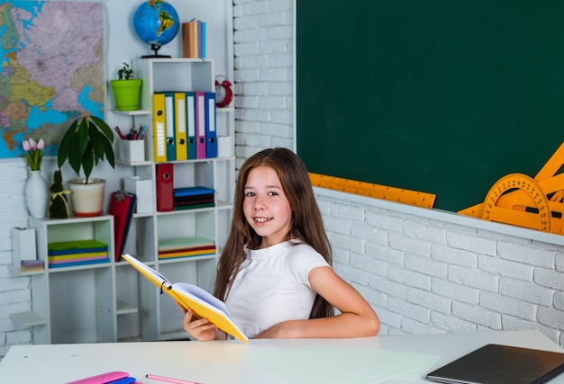 Niña adolescente sonriente leyendo un libro en la escuela de educación en el aula