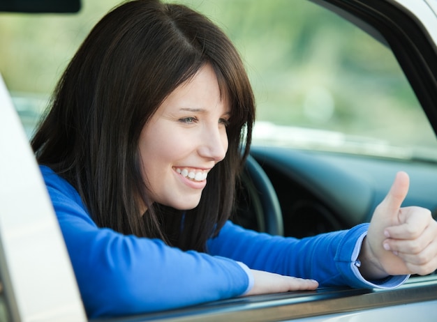 Niña adolescente sonriente con un pulgar hacia arriba sentado en su coche