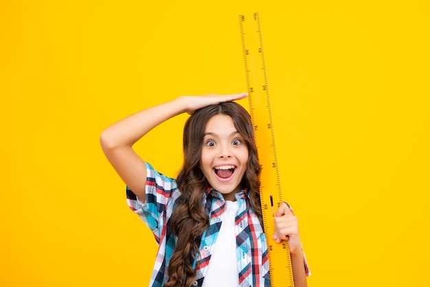 Niña adolescente sorprendida Midiendo el equipo escolar Colegiala sosteniendo la medida para la lección de geometría aislada sobre fondo amarillo Matemáticas de estudio estudiantil Expresión emocionada alegre y alegre