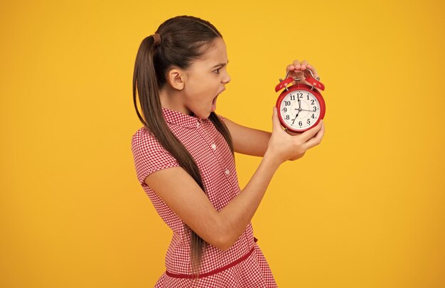 Niña adolescente triste infeliz Niño estudiante niña con reloj aislado sobre fondo amarillo Niño de regreso a la escuela Concepto de educación y tiempo