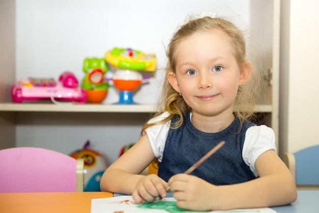 Niña adorable dibuja un pincel y pinta en la sala de guardería