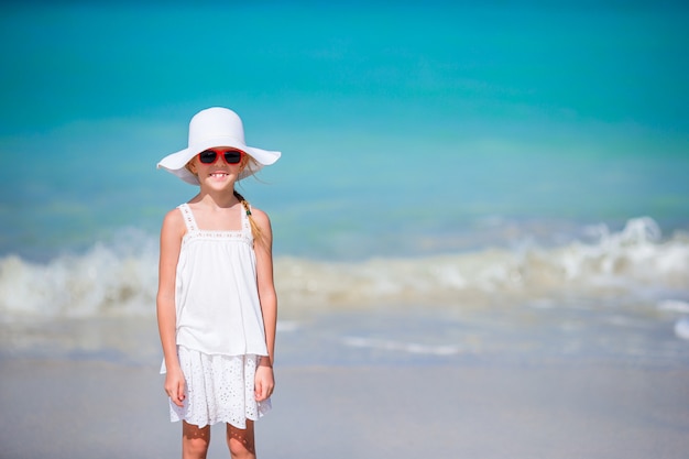 Niña adorable en gran sombrero rojo en la playa