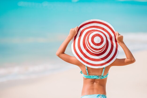 Niña adorable en gran sombrero rojo en la playa