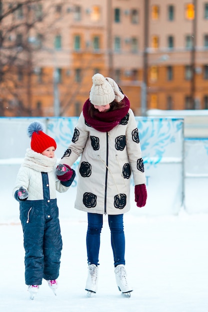 Niña adorable con madre patinando en pista de hielo con madre