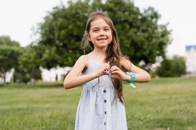 Niña adorable mostrando el corazón con las manos Niño lindo muestra paz y amor Niño feliz sonriendo y posando en el parque verde