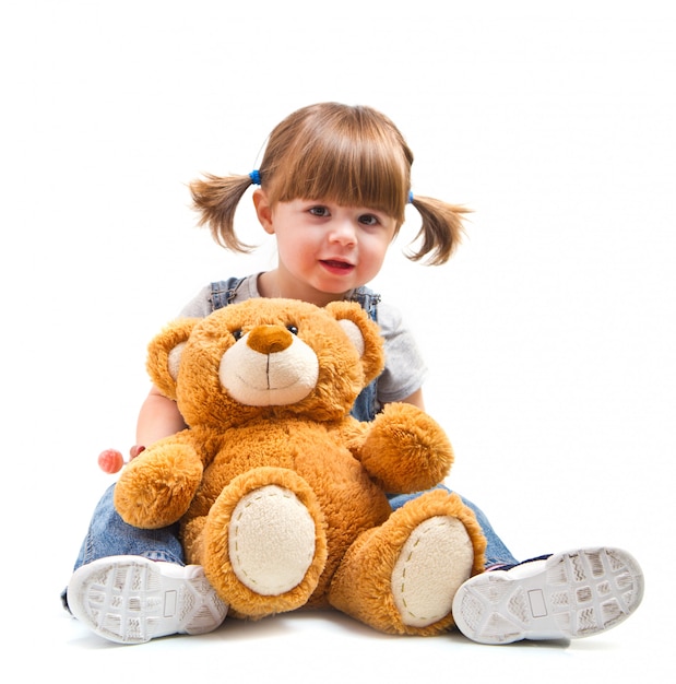 Niña adorable que abraza un oso de peluche