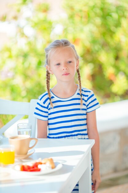 Niña adorable que desayuna en el café con vista al mar temprano en la mañana