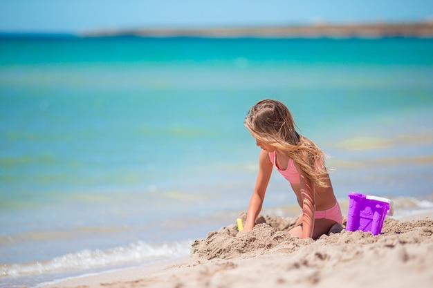 Niña adorable que juega con los juguetes de la playa durante vacaciones tropicales