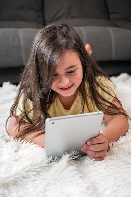 Niña adorable que usa una tableta digital en el piso en casa