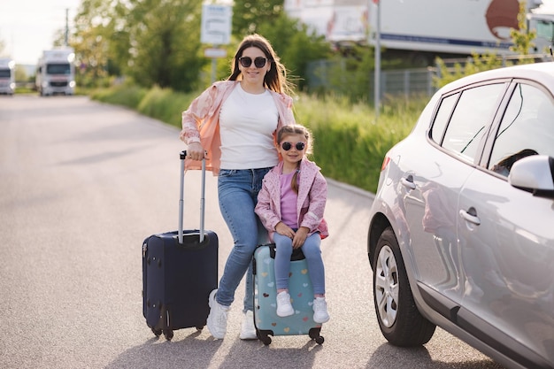 Una niña adorable se sienta en la maleta de su hijo y espera el viaje con su madre Dos hermosas niñas se preparan