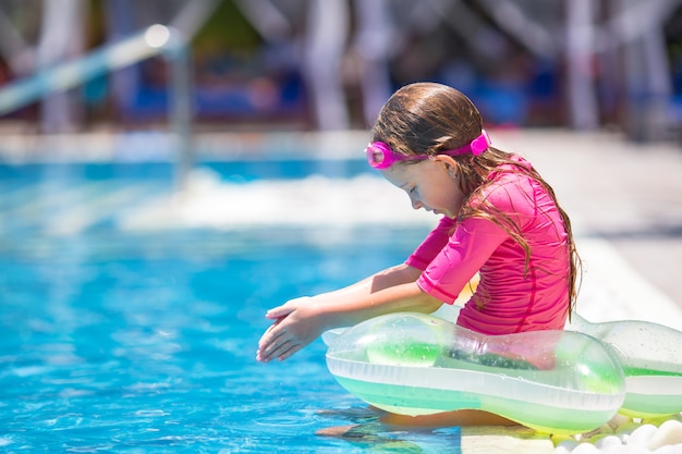 Niña adorable sonriente divirtiéndose en la piscina al aire libre