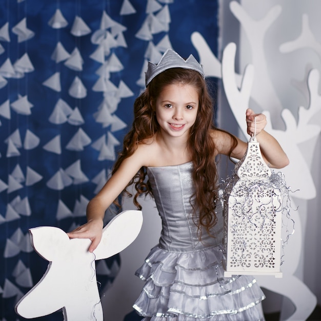 Niña en adornos navideños. Retrato de niña hermosa con pelo largo y rizado con corona