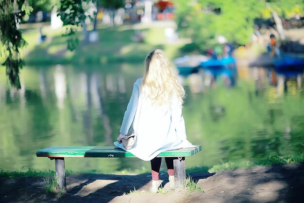 niña adulta sentada en un banco en el parque / bella modelo mujer descansando en un banco, alegre niña feliz