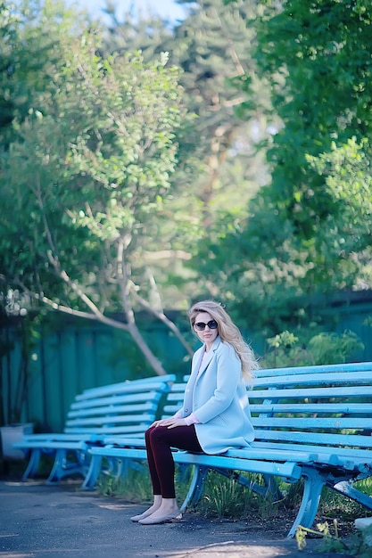 niña adulta sentada en un banco en el parque / bella modelo mujer descansando en un banco, alegre niña feliz