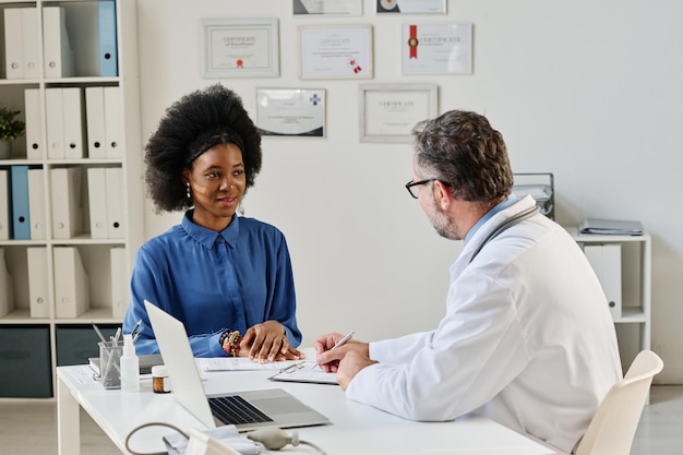 Foto niña africana hablando con el médico en la mesa durante su visita a su oficina