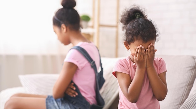 Niña africana llorando en casa siendo ignorada por su hermana mayor