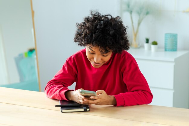 Niña africana con pantalla táctil de teléfono inteligente escribiendo página de desplazamiento en casa mujer con teléfono celular