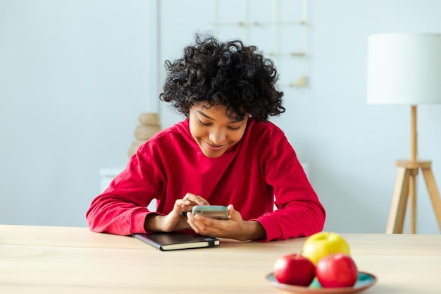 Niña africana con pantalla táctil de teléfono inteligente escribiendo página de desplazamiento en casa mujer con teléfono celular