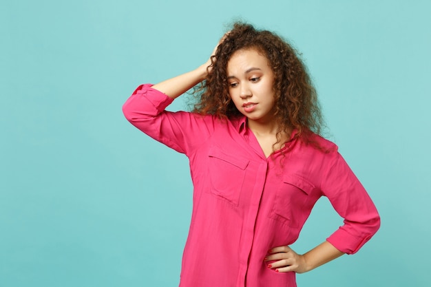 Niña africana preocupada en ropa casual rosa mirando hacia abajo, poniendo la mano en la cabeza aislada sobre fondo de pared azul turquesa en estudio. Personas sinceras emociones, concepto de estilo de vida. Simulacros de espacio de copia.