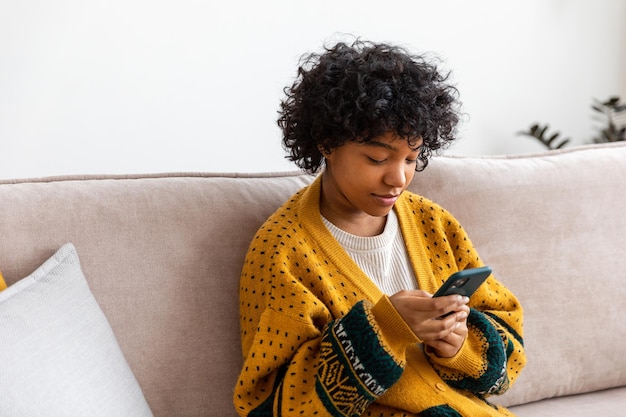 Niña africana sosteniendo la pantalla táctil del teléfono inteligente escribiendo la página de desplazamiento en casa Mujer con teléfono celular navegando por Internet usando aplicaciones de redes sociales jugando Compras en línea Noticias de Internet Adicción al teléfono celular