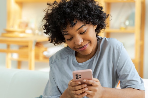 Niña africana sosteniendo la pantalla táctil del teléfono inteligente escribiendo la página de desplazamiento en casa mujer con teléfono celular surfeando