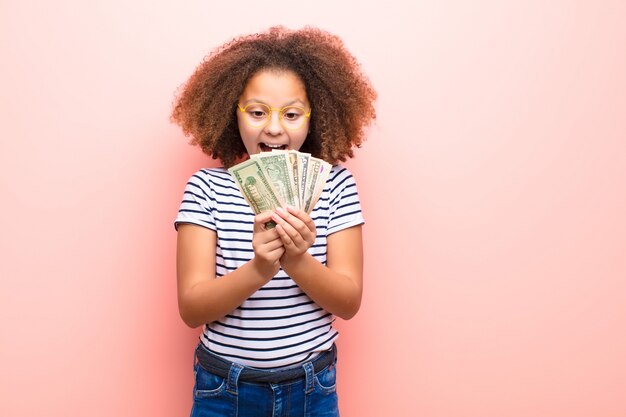 Niña afroamericana contra la pared plana con billetes de dólar