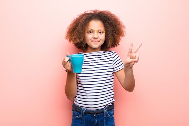 Niña afroamericana contra la pared plana con una taza de café