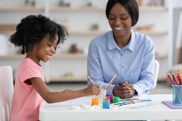 Niña afroamericana creativa pintando con especialista en niños