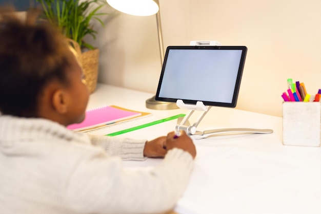 Niña afroamericana feliz aprendiendo, usando tableta con copia en casa