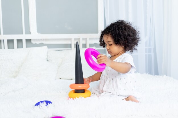 Niña afroamericana juega y recoge una pirámide colorida en casa en la cama