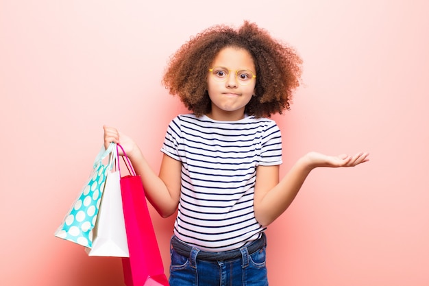 Niña afroamericana en pared plana con bolsas de compras