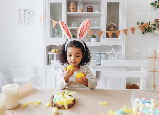 Niña afroamericana pinta huevos de Pascua en casa en la cocina felices pascuas