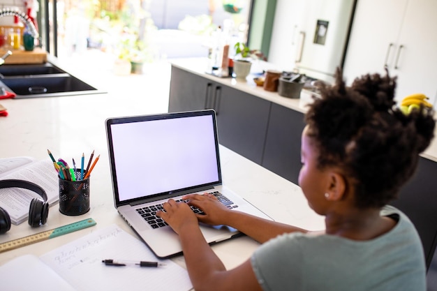 Niña afroamericana que usa una computadora portátil mientras aprende en línea en casa, copia espacio