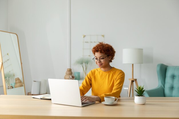 Niña afroamericana que usa una computadora portátil en la oficina en casa mirando la pantalla escribiendo chateando leyendo escribiendo correo electrónico Mujer joven que tiene una reunión virtual chat en línea videollamada conferencia Trabajo aprendiendo desde casa