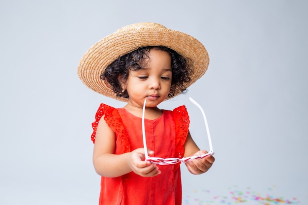 Niña afroamericana en ropa roja de verano y un sombrero de paja sobre un fondo blanco en el estudio