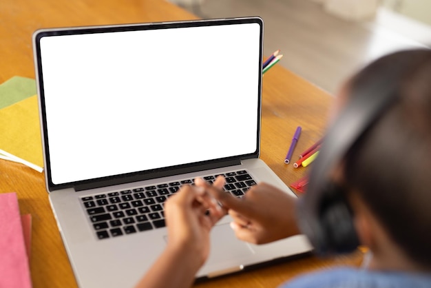 Niña afroamericana sentada en una mesa usando una computadora portátil con espacio de copia para una lección en línea