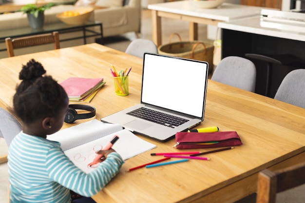 Niña afroamericana sentada en una mesa usando una computadora portátil con espacio de copia para una lección en línea