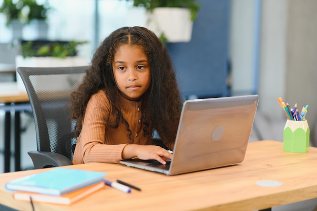 Niña afroamericana sentada en la mesa usando una computadora portátil para una lección en línea
