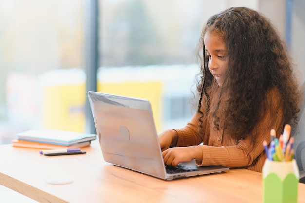 Niña afroamericana sentada en la mesa usando una computadora portátil para una lección en línea
