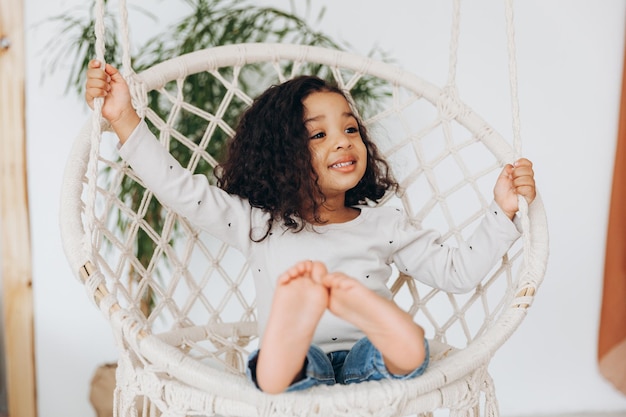 Niña afroamericana en una silla de mimbre colgada en la sala de estar