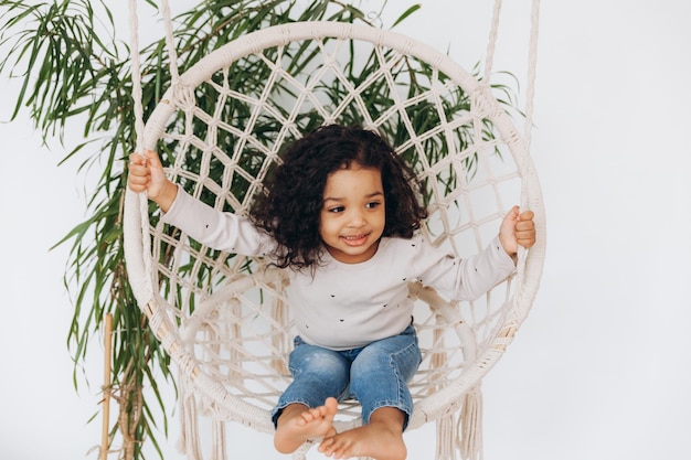 Niña afroamericana en una silla de mimbre colgada en la sala de estar