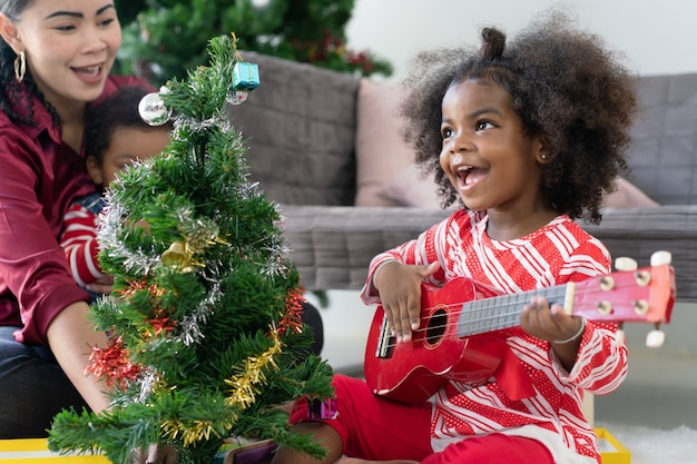 Niña afroamericana tocando la guitarra ukelele celebró la Navidad en casa con su madre