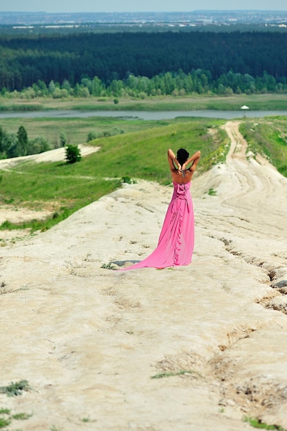 Una niña afroamericana con un vestido rosa se para en la colina con las manos detrás de la cabeza