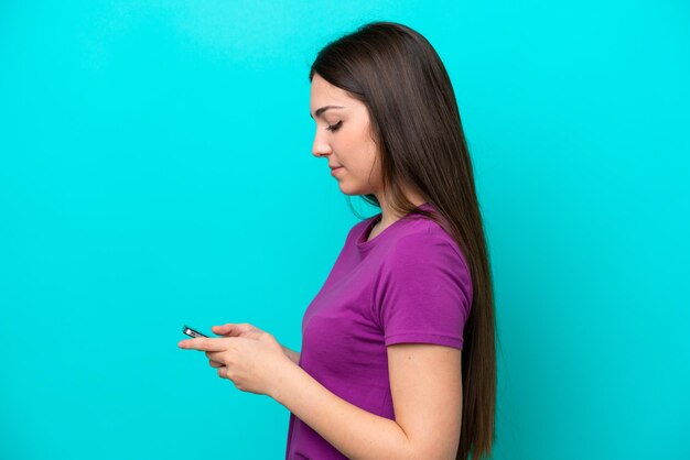 Niña aislada de fondo azul enviando un mensaje o correo electrónico con el móvil