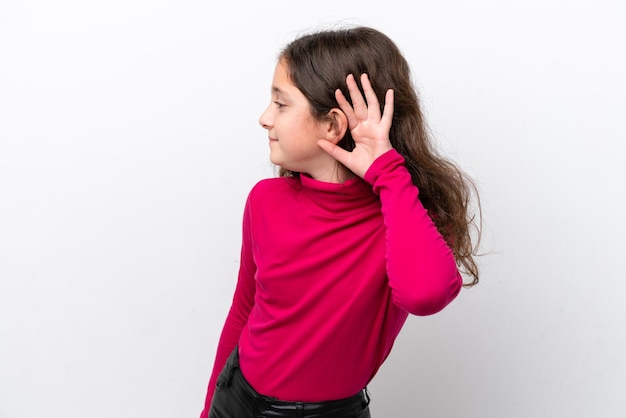 Niña aislada de fondo blanco escuchando algo poniendo la mano en la oreja