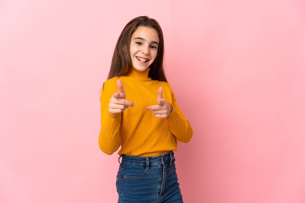 Niña aislada en la pared rosa apuntando hacia el frente y sonriendo